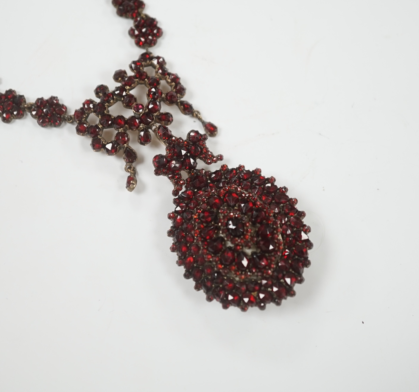 A Victorian gilt metal and facet cut garnet cluster set mourning drop pendant necklace, overall 50cm.